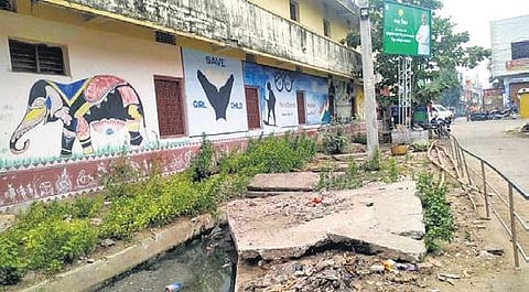 The broken cement slabs lying beside the uncovered drains.