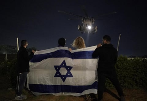 People holding an Israeli flag watch the arrival of a helicopter transporting Israeli hostages released by Hamas at the Sheba Medical Center in Ramat Gan, Israel. (Photo | AP)