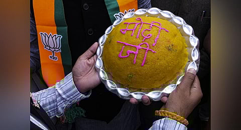 A BJP worker carries a sweet dish during celebrations at the party headquarters in New Delhi, Sunday, Dec. 3, 2023. (PTI Photo)
