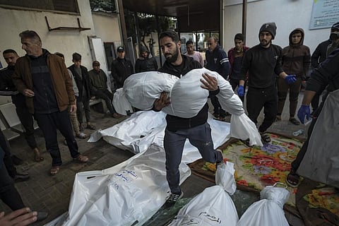 A Palestinian man carries the body of his relative killed in the Israeli bombardment of the Gaza Strip, outside a morgue in Rafah, southern Gaza, Friday, Dec. 29, 2023. | AP