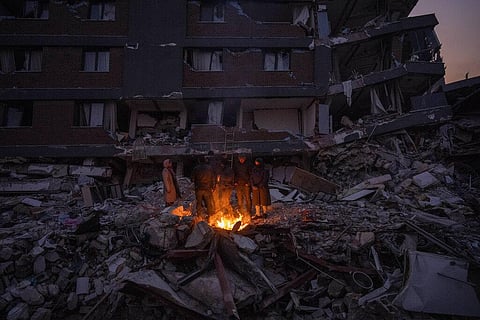 Members of a family warm themselves around a campfire in front of a building where five members of their family were fatally trapped in Antakya, Turkey, Feb. 12, 2023. (Photo | AP)