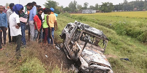 Villagers watch a burnt car which ran over and killed farmers on Sunday, at Tikonia village in Lakhimpur Kheri, Uttar Pradesh. (File Photo | AP)