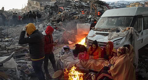 Survivors gather next to a bonfire outside collapsed buildings after their homes were destroyed in a 7.8 magnitude earthquake which struck the border region of Turkey and Syria. (Photo | AFP)