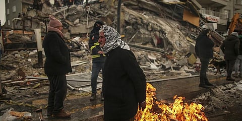 People warm themselves next to a collapsed building in Malatya, Turkey. (File photo | AP)