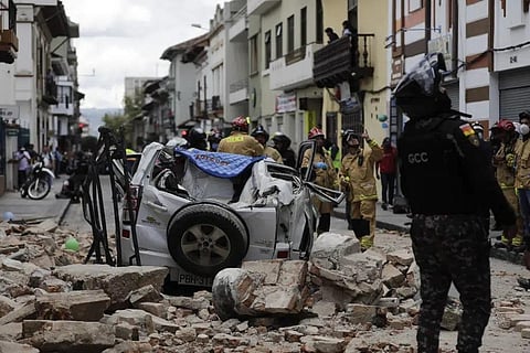 A police officer looks up next to a car crushed by debris after an earthquake shook Cuenca, Ecuador, Saturday, March 18, 2023. (Photo | AP)