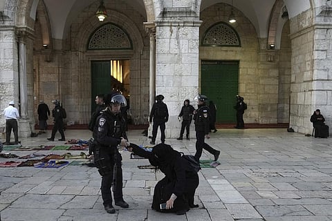 An Israeli policewoman pulls up a woman worshipper who was sitting on the ground at the Al-Aqsa Mosque compound following a raid at the site during Ramadan. (Photo | AP)