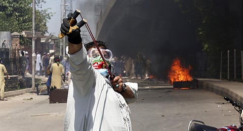 A supporter of Pakistan's former PM Imran Khan throws stones using a slingshot toward police officers during a protest against the arrest of their leader in Peshawar, Pakistan, Wednesday, May 10.(AP)