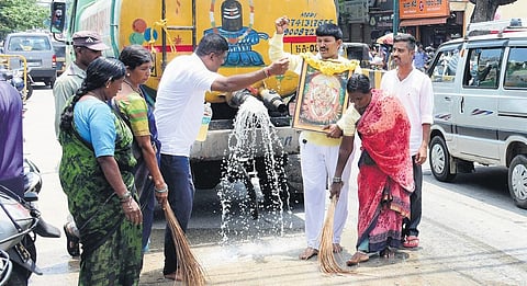 Kamsale Ravi cleans a part of the Jamboo Savari route with water, gomutra and cow dung in Mysuru on Sunday. (Photo|Udayashankar S)