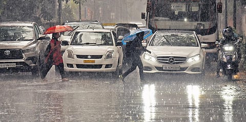 People cross a road as vehicles wait during heavy showers in Bengaluru on Friday | Vinod Kumar T