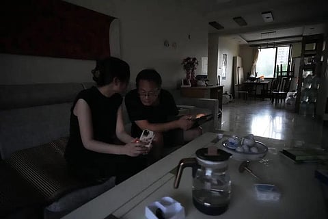 Wang Quanzhang and his wife Li Wenzu chat while looking through their phone & laptop after power was cut off for their apartment in Beijing's Changping district, June 20, 2023. (Photo | AP)