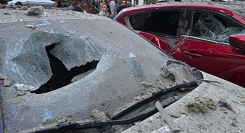 People stand at a parking with damaged cars in front of a multi-story apartment building after Russian attack in Kyiv, Ukraine. (Photo | AP)