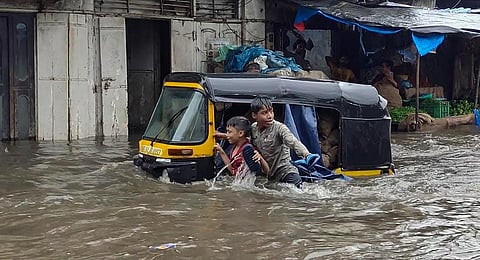 Children wade through a flooded street following heavy rainfall at Bhiwandi in Thane district. (Photo | PTI)