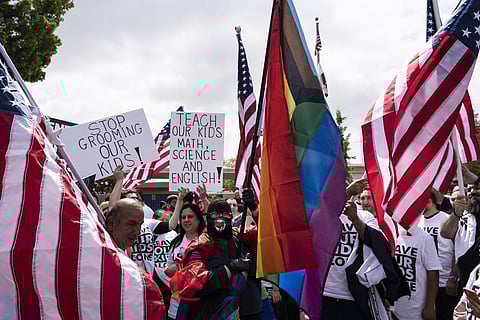 A woman draped in Pride flags is surrounded by people protesting a planned Pride month assembly outside Saticoy Elementary School in Los Angeles. (Photo |AP)