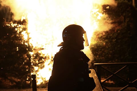 A riot police officer is silhouetted as he walks in front of a fire on the third night of protests sparked by the fatal police shooting of a 17-year-old. (Photo | AP)