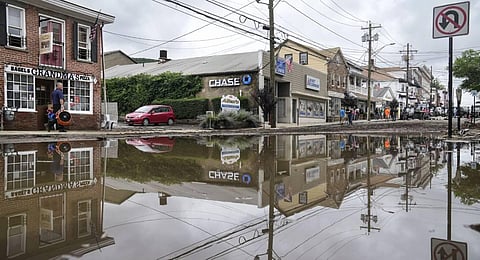 Residents, journalists, and emergency service workers walk around a flooded Main Street. (Photo | AP)