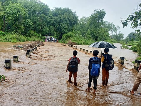 Schoolchildren try to cross a flooded bridge at Kamabarganavi village in Dharwad district, Karnataka. (Express)