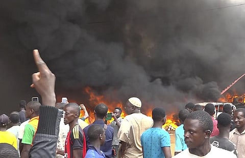 With the headquarters of the ruling party burning in the back, supporters of mutinous soldiers demonstrate in Niamey, Niger. (Photo | AP)
