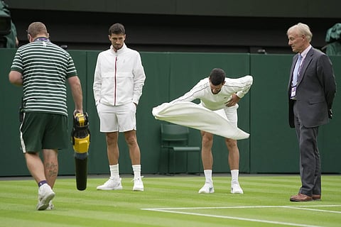 A member of the ground staff uses a leaf blower and Serbia's Novak Djokovic wafts his towel to assist with drying the court as Pedro Cachin looks on at Wimbledon, July 3, 2023. (Photo | AP)