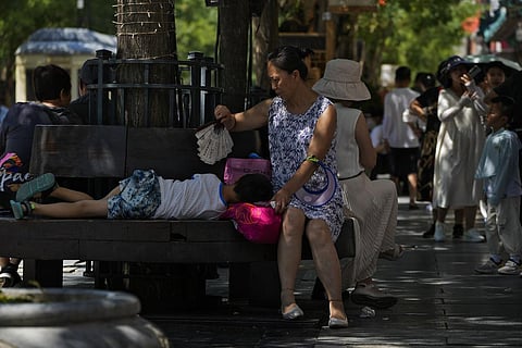 A woman uses a fan to cool a child as they sit on a bench at Qianmen pedestrian shopping street on a hot day in Beijing. (Photo | AP)