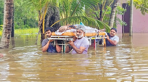 A sick elderly man being carried on a stretcher to a hospital through chest-deep water at Nedumbram near Tiruvalla on Thursday. The Manimalayar breached its banks following heavy rain causing flooding