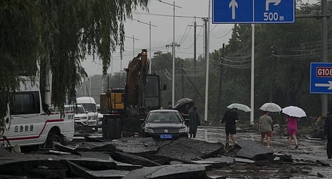 People and vehicles pass through a road damaged by floodwaters in the Mentougou district as continuous rainfall triggers alerts in Beijing, Monday, July 31, 2023. (AP Photo)