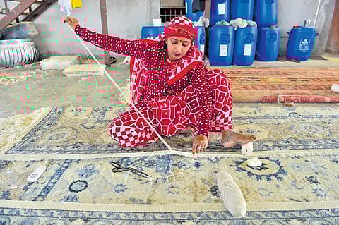 A woman gives final touches to a rug;
