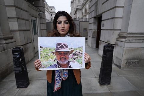 FILE - Roxanne Tahbaz holds a picture of her father Morad Tahbaz who is jailed in Iran, during a protest outside Foreign, Commonwealth and Development Office in London, April 13, 2022. (Photo | AP)