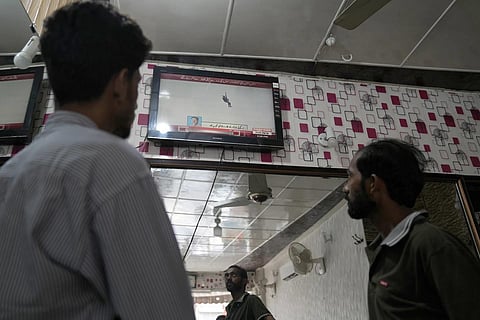 People watch a news channel airing news regarding people trapped in a cable car, at a barner shop in Lahore, Pakistan. (Photo | AP)