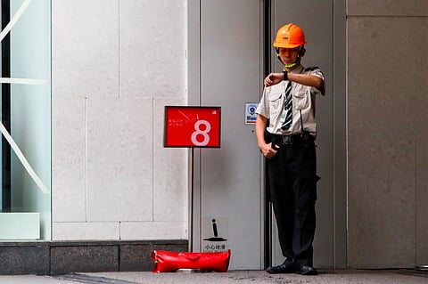 A security person wearing a hard hat checks his watch near a sign marking the No. 8 typhoon signal outside a shopping mall as Super Typhoon Saola approaches Hong Kong. (Photo | AP)