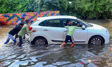 Young men push a car after it broke down on waterlogged road after heavy rainfall, in Mathura. (Photo | PTI)