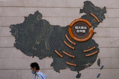 FILE - A woman walks past a map showing Evergrande development projects in China, at an Evergrande city plaza in Beijing on Sept 21, 2021. (Photo | AP)
