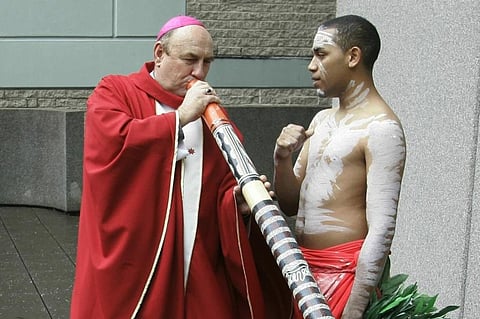 FILE - Bishop Christopher Saunders of Broome tries to play a digeridoo during a World Youth Day 2008 media event in Sydney, Australia, on April 17, 2008. (Photo | AP)