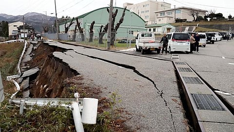 People stand next to large cracks in the pavement after evacuating into a street in the city of Wajima, Ishikawa prefecture on January 1, 2024. (AFP)