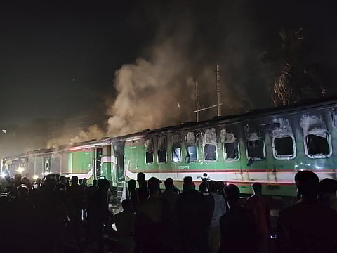People stand near a burning passenger train at Gopibagh in Dhaka, Bangladesh, Friday, Jan. 5, 2024. (Photo | AP)