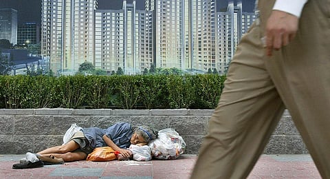 A homeless woman sleeps with her belongings beneath an advertising billboard promoting new urban development, 21 August 2003 in Beijing, as a man walks past. (File Photo | AFP)