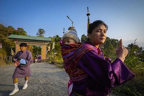 A Bhutanese woman carrying her child on her back shows the voting mark on her index finger after casting her vote, Tuesday, Jan 9, 2024. (Photo | AP)