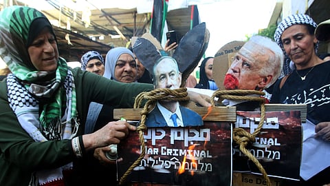 A woman stands next to the image of Israeli Prime Minister Benjamin Netanyahu (L) and US President Joe Biden (R) before they are set alight during a protest in the Ain al-Hilweh Palestinian refugee camp near the southern Lebanese port city of Sidon on October 18, 2023.
