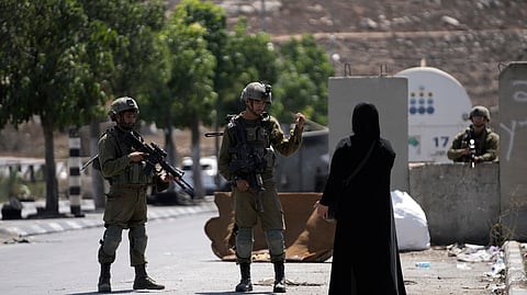Israeli soldiers speak to a Palestinian woman near Beit Hagai, a Jewish settlement in the hills south of the large Palestinian city of Hebron, near Jerusalem, on Wednesday, Aug. 30, 2023.