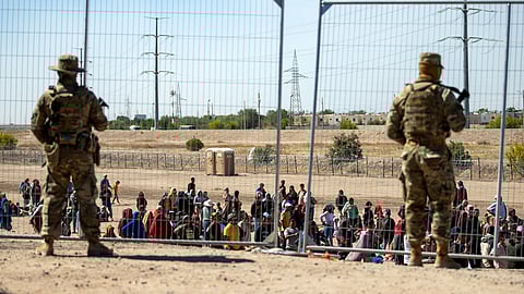 Migrants wait in line adjacent to the border fence under the watch of the Texas National Guard to enter into El Paso, Texas, May 10, 2023.