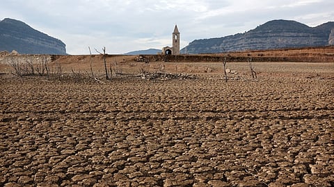 This photograph taken on January 15, 2024 shows the dry soil next to the low water-level reservoir of Sau with in background Sant Roma de Sau church, in the province of Girona in Catalonia.