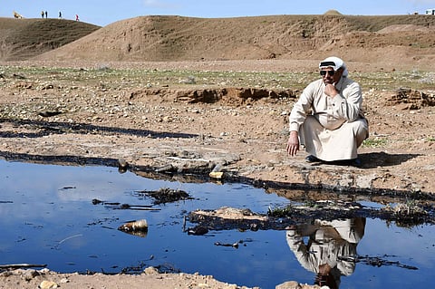 An Iraqi farmer squats and checks an oil spill into an agricultural land in the region of Hamrin, north of Tikrit, in the province of Salaheddin.