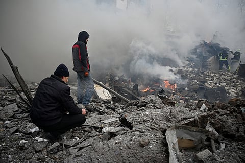 Local residents stand among debris as Ukrainian firefighters work at the site of a missile attack in Kharkiv on January 23, 2024.