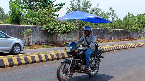 As temperature rises with the onset of summer a man riding a motorcycle with a bike umbrella fitted on it, to get rid of heat.