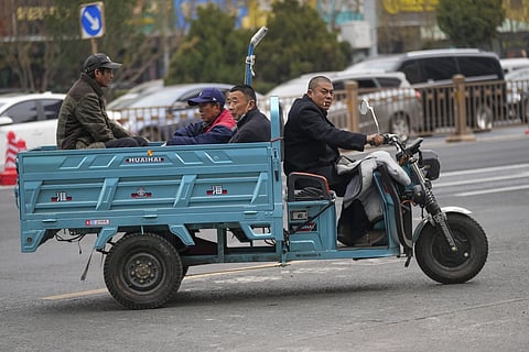 Workers sit on a three-wheeled bike on the street in Beijing, March 21, 2024.