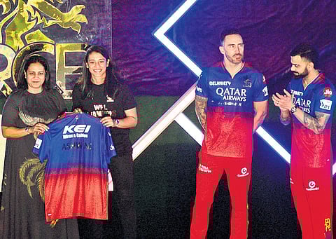 RCB captain Faf du Plessis, cricket icon Virat Kohli, and RCB Women’s team captain Smriti Mandhana along with Ashwini Puneeth Rajkumar unveil the new jersey during the RCB Unbox event at Chinnaswamy Stadium in Bengaluru on Tuesday. The team also changed its name to Royal Challengers Bengaluru before the Indian Premier League 2024.