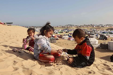 Palestinian children play on a sand dune overlooking a camp for displaced people in Rafah in the southern Gaza Strip on March 17, 2024, amid ongoing battles between Israel and the militant group Hamas.
