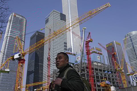 A man smokes as he walks by a construction site near office buildings in the Central Business District in Beijing on Saturday, March 2, 2024.