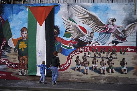 A woman and a child walk, during the unveiling of the International Wall, after it was transformed into a Gaza Mural, in Belfast, Sunday, March 3, 2024.