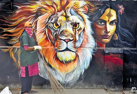 A sanitation worker sweeps the area near a mural by Dhruva Art Academy on MG Road