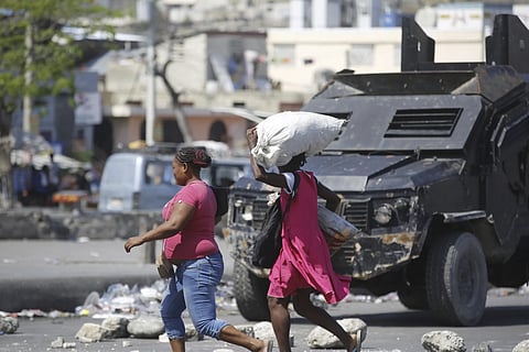 Pedestrians run past an armored police car in Port-au-Prince, Haiti, Thursday, March 7, 2024.